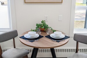 A dining table with two white bowls, two plates, and two forks, set with dark blue placemats. There is a potted plant with green leaves on the table. - Downtown Edmonton Studio | AC, Parking (Edmonton)