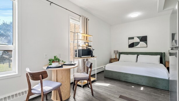 Et moderne hotelværelse med seng, skrivebord med computer, stole og udsigt til det fri.