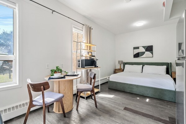 Habitació d'hotel moderna amb llit, escriptori amb ordinador, cadires i vista a l'exterior.