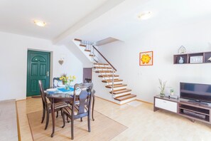 Ein Essbereich mit Tisch und Stühlen, einer Treppe, einem Fernseher und einem Regal mit Dekoration.