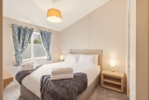 A bedroom with a bed, bedside tables, a window with curtains, and a hanging light fixture. - Cheviot Retreat Lodge - North East Escapes (Wooler)