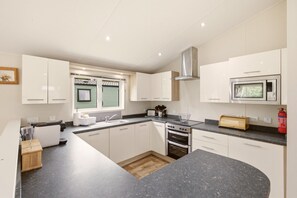 A modern kitchen with white cabinets, a built-in oven, a microwave, and a large island with a sink. - Cheviot Retreat Lodge - North East Escapes (Wooler)