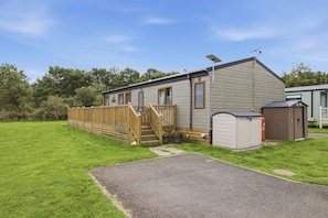 A single-story mobile home with a wooden deck, a small porch, and a shed. - Cheviot Retreat Lodge - North East Escapes (Wooler)