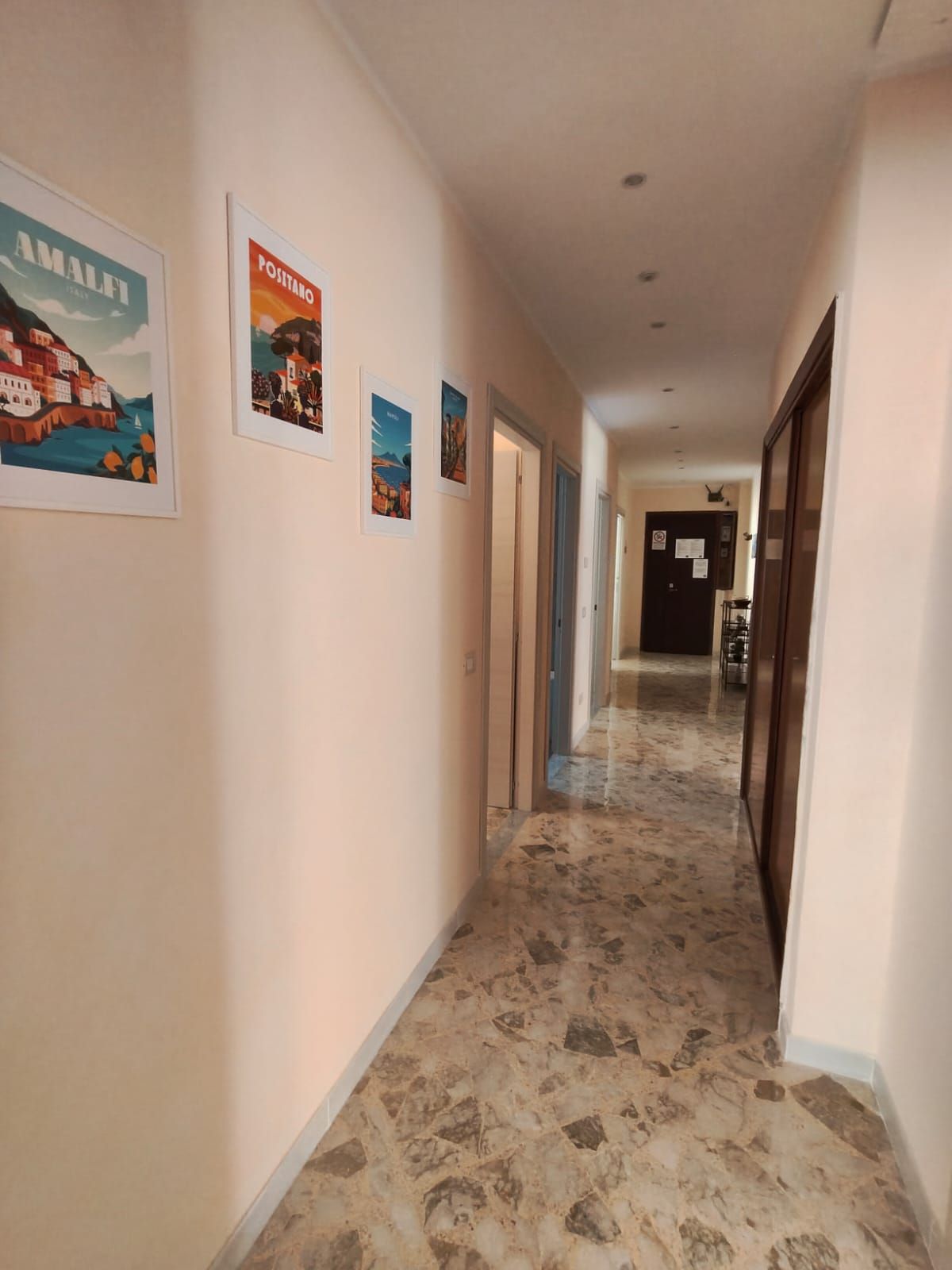 Ein Hotelgang mit gerahmten Kunstwerken an den Wänden und einem Marmorboden.