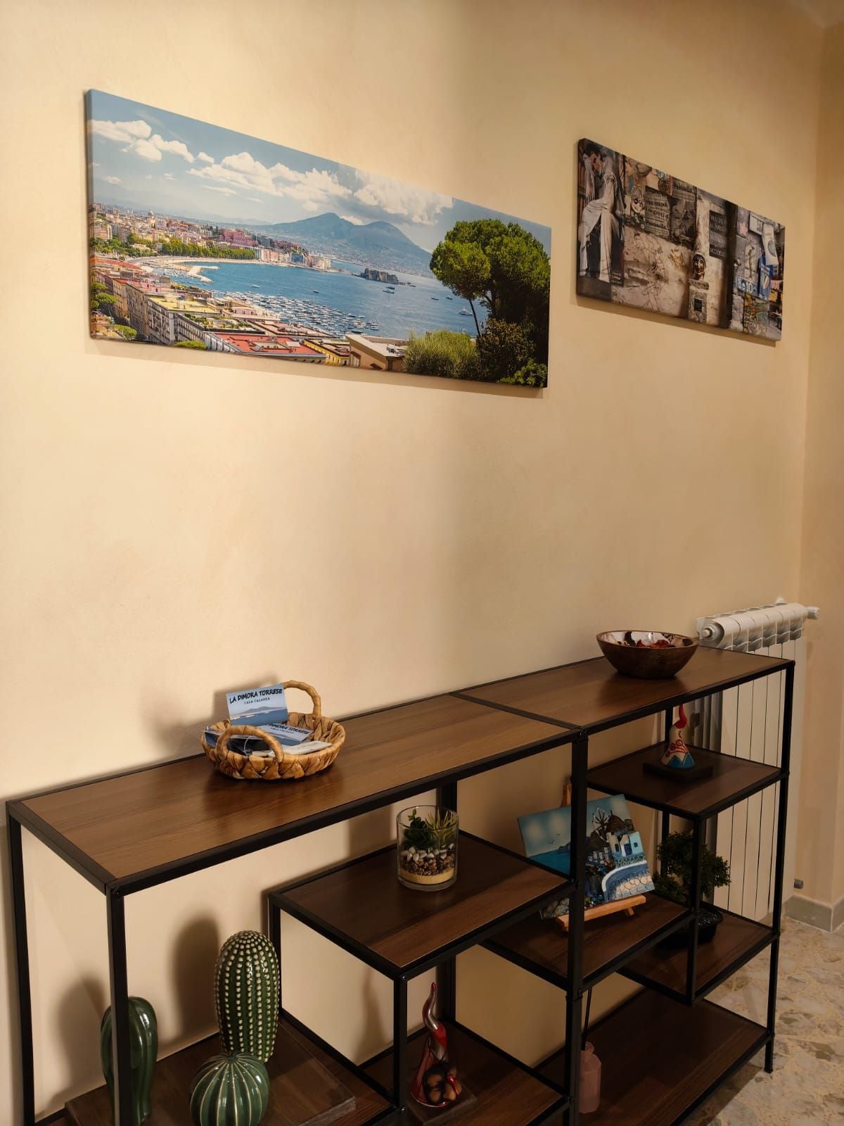 Una stanza con un tavolino consolle in legno, un quadro di un paesaggio con cornice e un elemento decorativo a parete.