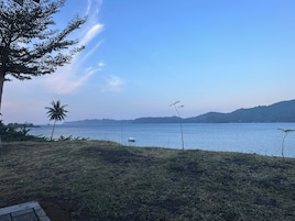 A grassy area with a body of water, a boat, and distant hills.