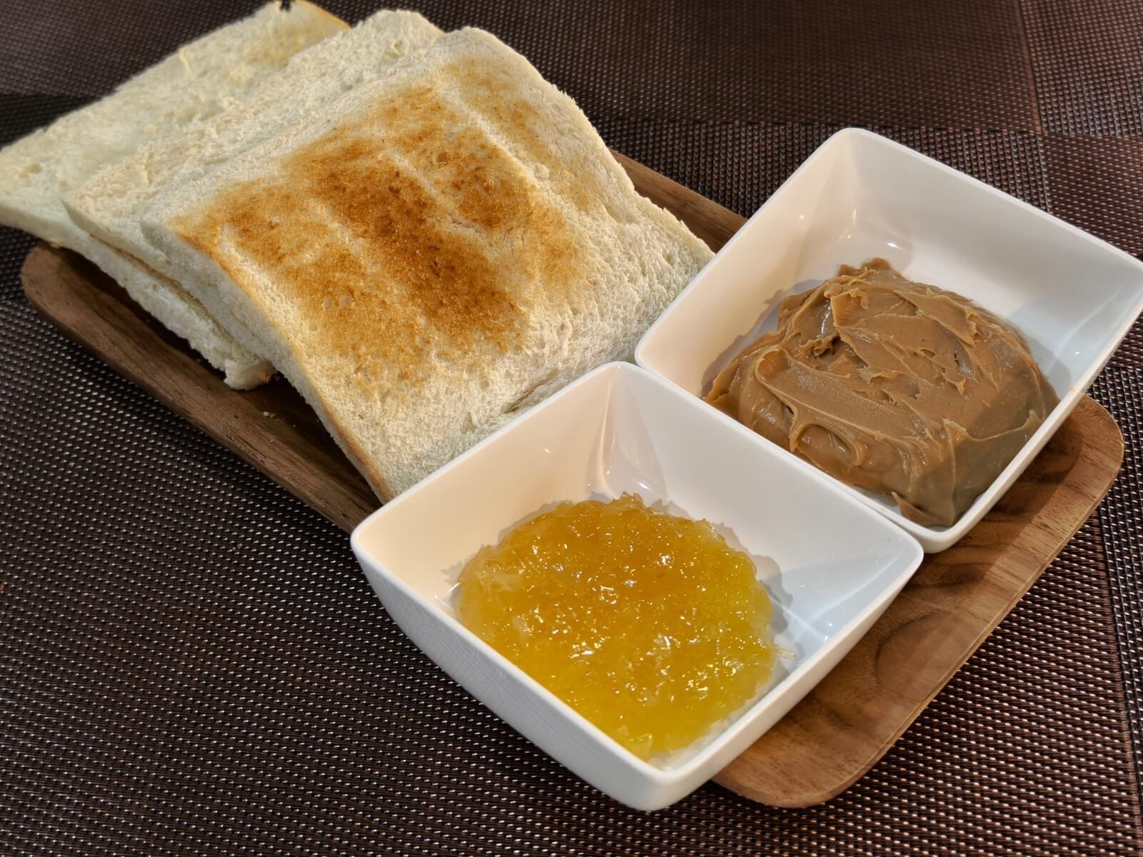 A wooden serving tray with toasted bread, peanut butter, and jam.