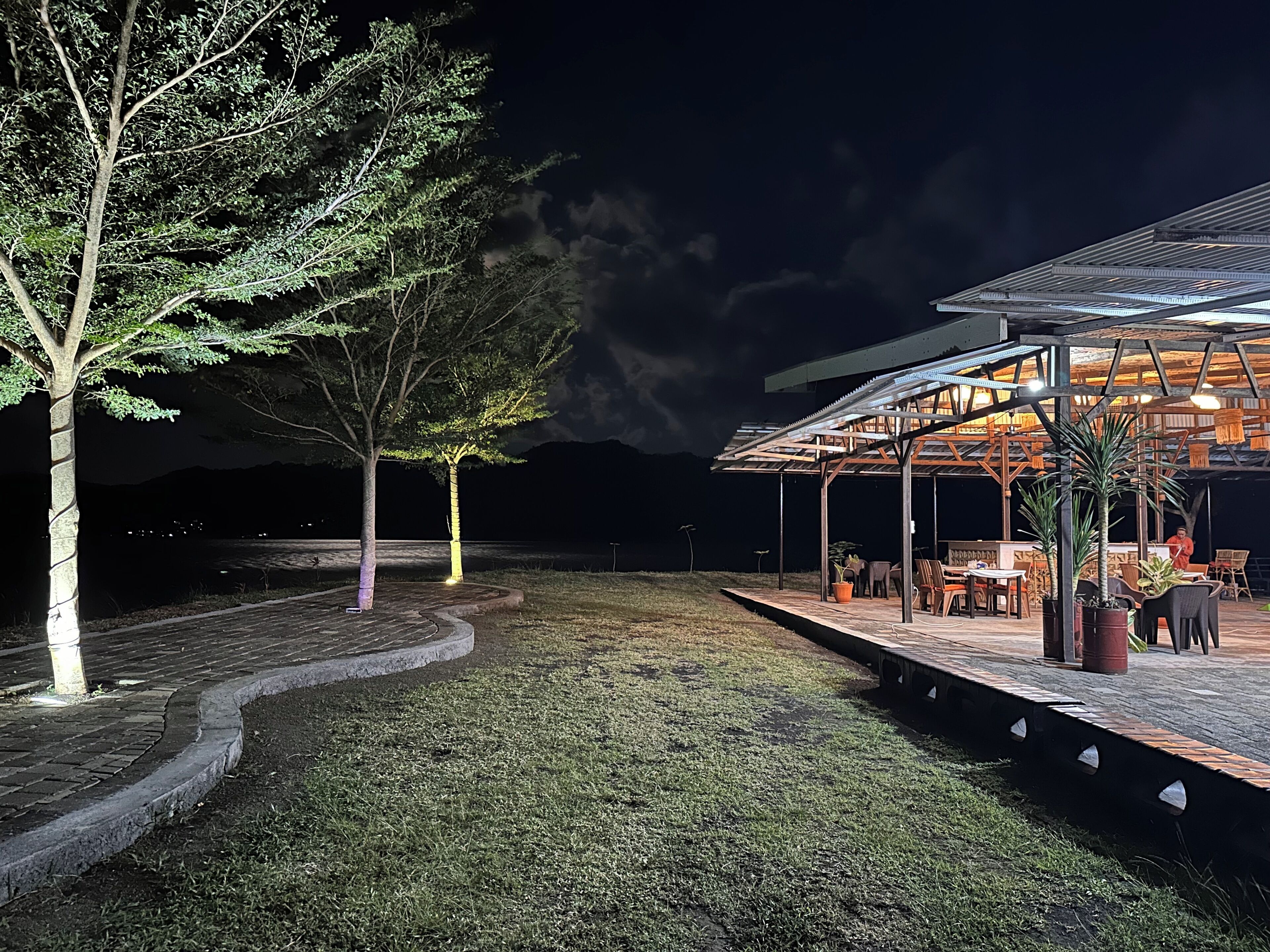 An outdoor seating area with tables and chairs, a covered structure, and trees.