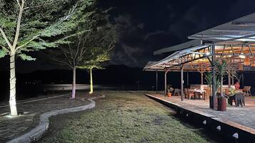 An outdoor seating area with tables and chairs, a covered structure, and trees.
