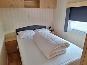 Una cama individual con ropa de cama blanca, una mesita de noche con lámpara y una ventana con persiana.