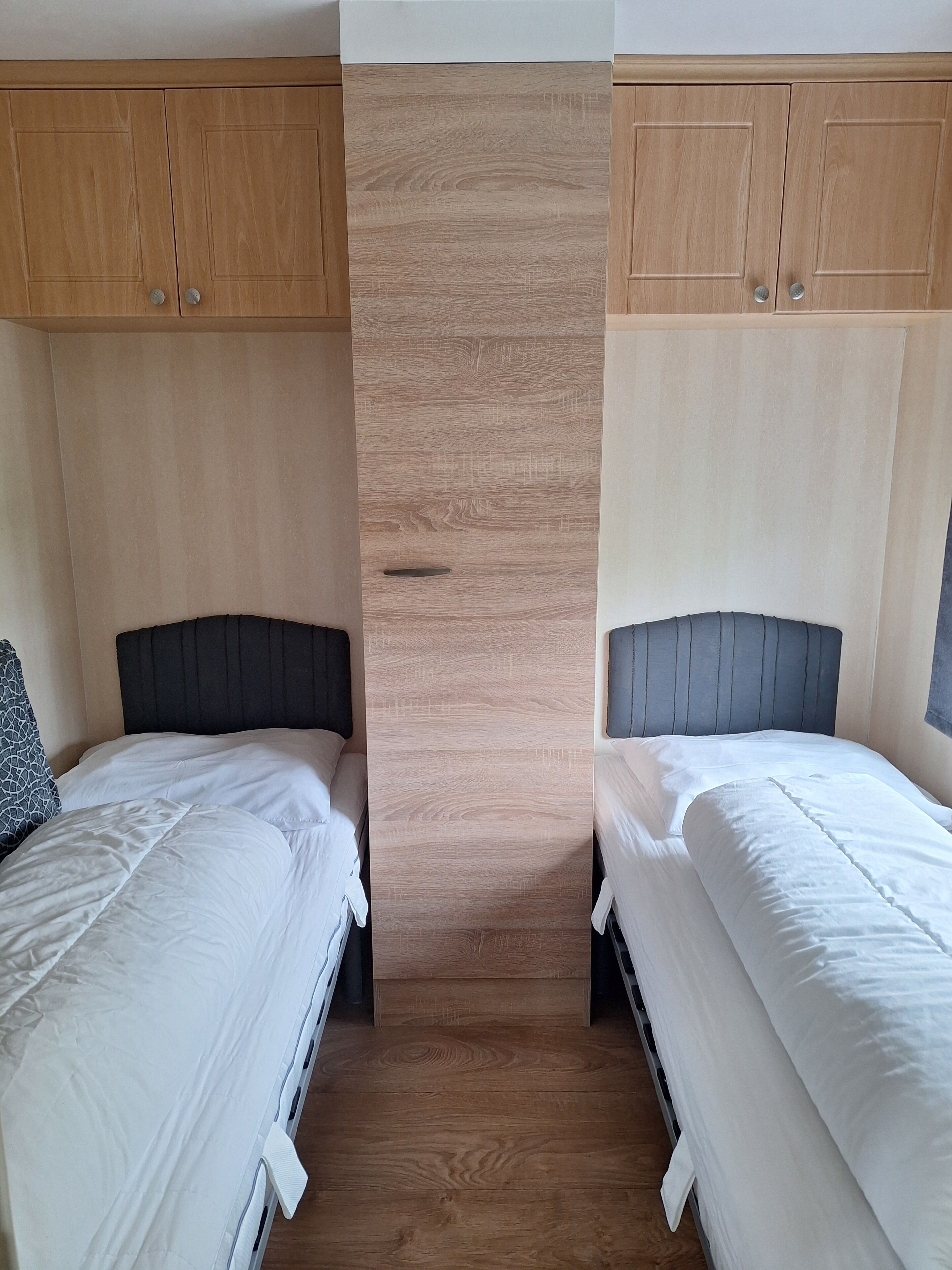 Ein Zimmer mit zwei Betten, Holzschränken und einer zentralen Wandverkleidung.