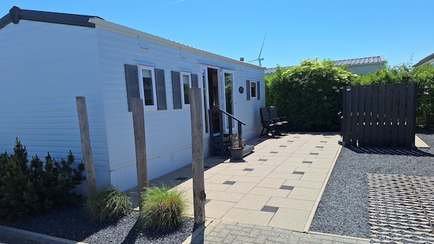 En hvid campingvogn med terrasse, et træhegn og en lille have.