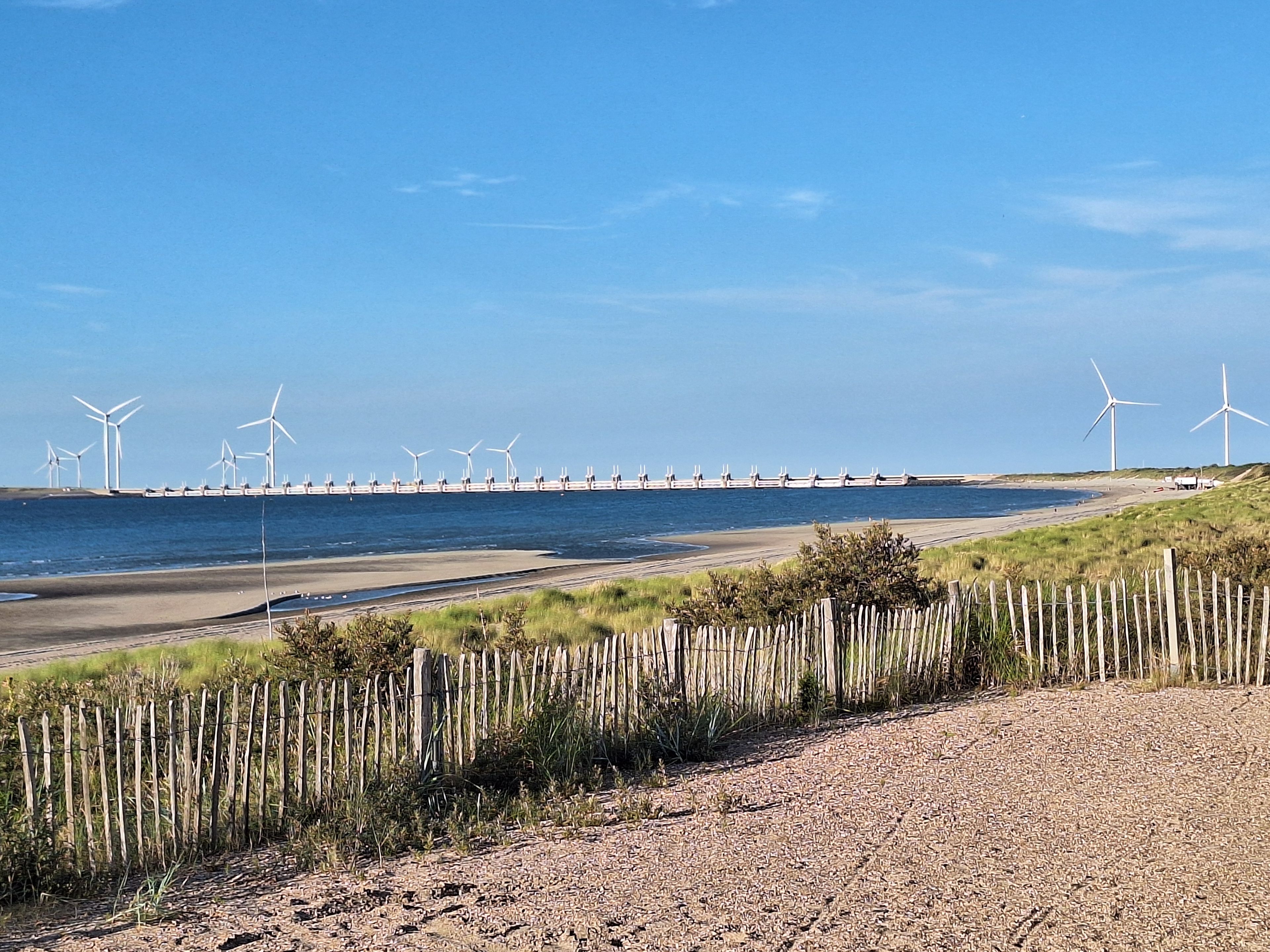 Eine Küstenlandschaft mit Windkraftanlagen, einem Sandstrand und einem Holzzaun.