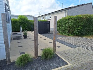 A residential outdoor area with a paved patio, a wooden fence, and a wind turbine in the background.