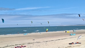 En strand med flere drager i luften, sand og hav i baggrunden.