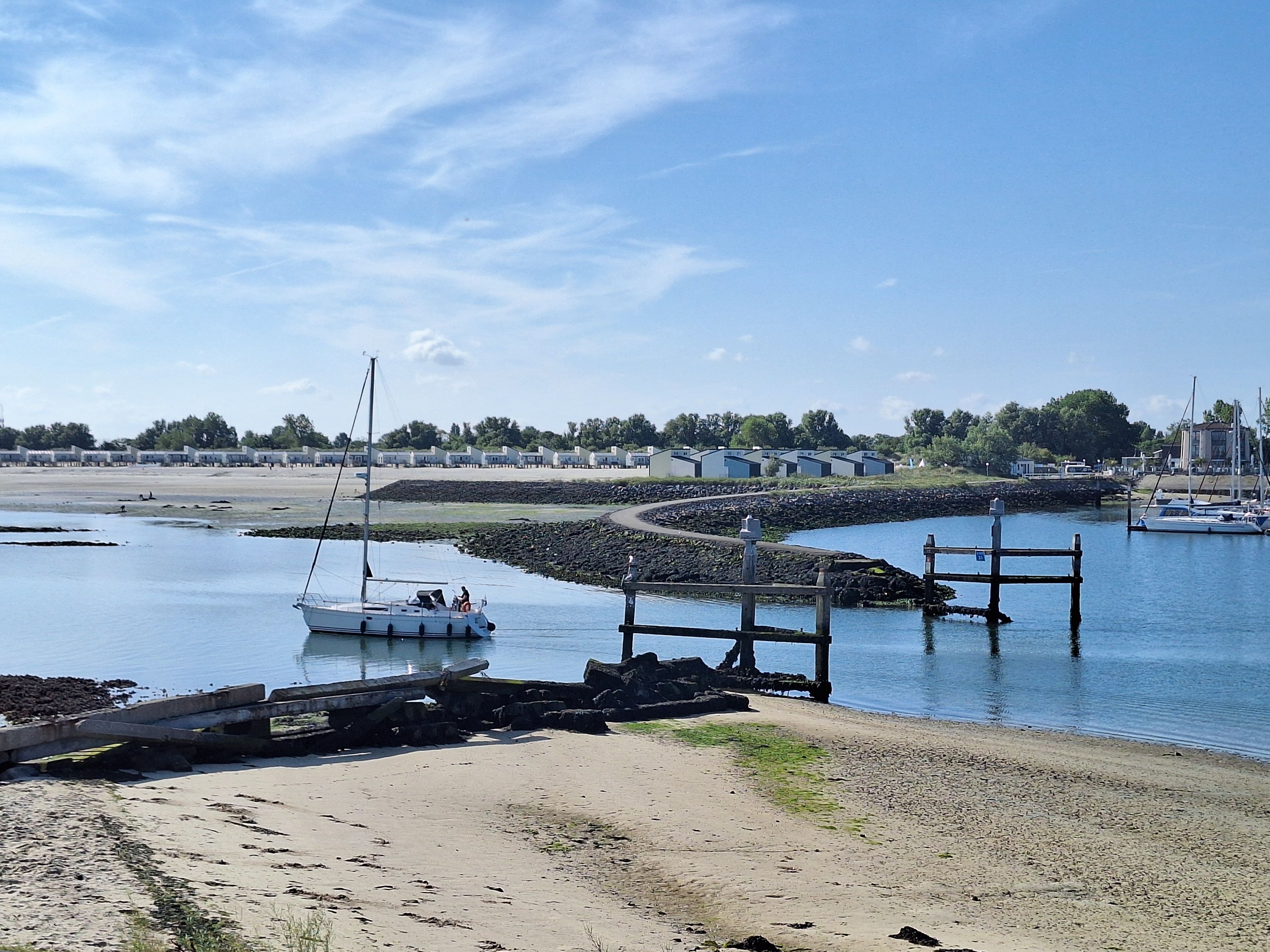 A marina with boats, a sandy beach, and a row of buildings in the background.