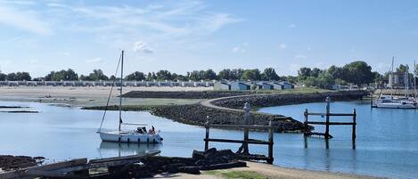 A marina with boats, a sandy beach, and a row of buildings in the background.