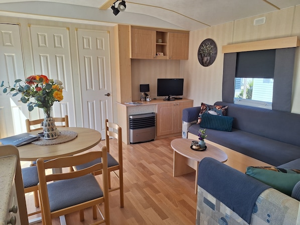 A compact living space with a dining area, a sofa, a television, and a window.