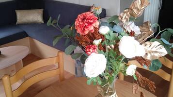 Ein Wohnzimmer mit einem dunkelblauen Sofa, einem Holzstuhl, einem Tisch mit Blumenvase und einem 'Welcome'-Schild.