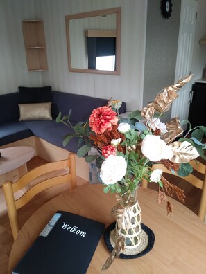 Una sala de estar con un sofá azul oscuro, una silla de madera, una mesa con un jarrón de flores y un letrero que dice 'Welcome'.
