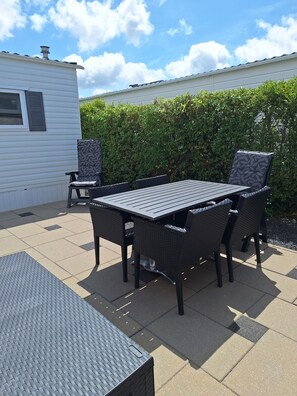 En uteplats med ett bord och stolar, ett litet, delvis överbyggt sittområde och en häck i bakgrunden.
