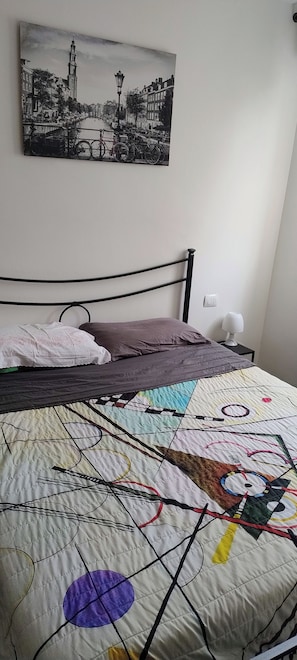 A bed with a quilt, a pillow, and a bedside table with a lamp. - Vrbo Property (Lido di Pomposa)