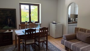 A dining area with a table and chairs, a small refrigerator, a sofa, and a painting on the wall.