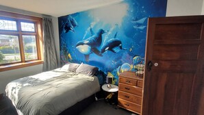 Quarto com cama, cômoda, janela e um mural de golfinhos.