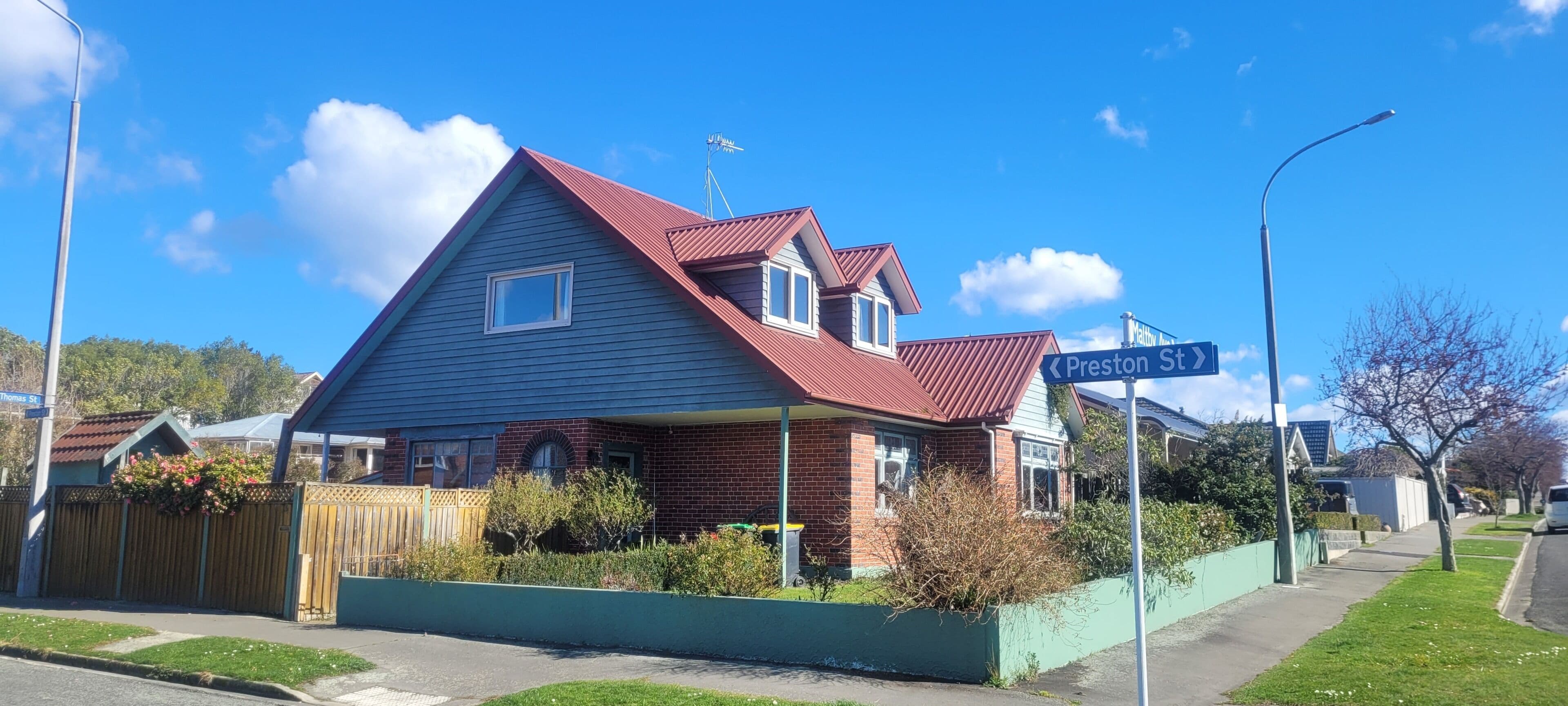 A two-story house with a red roof, a front porch, and a green front yard.