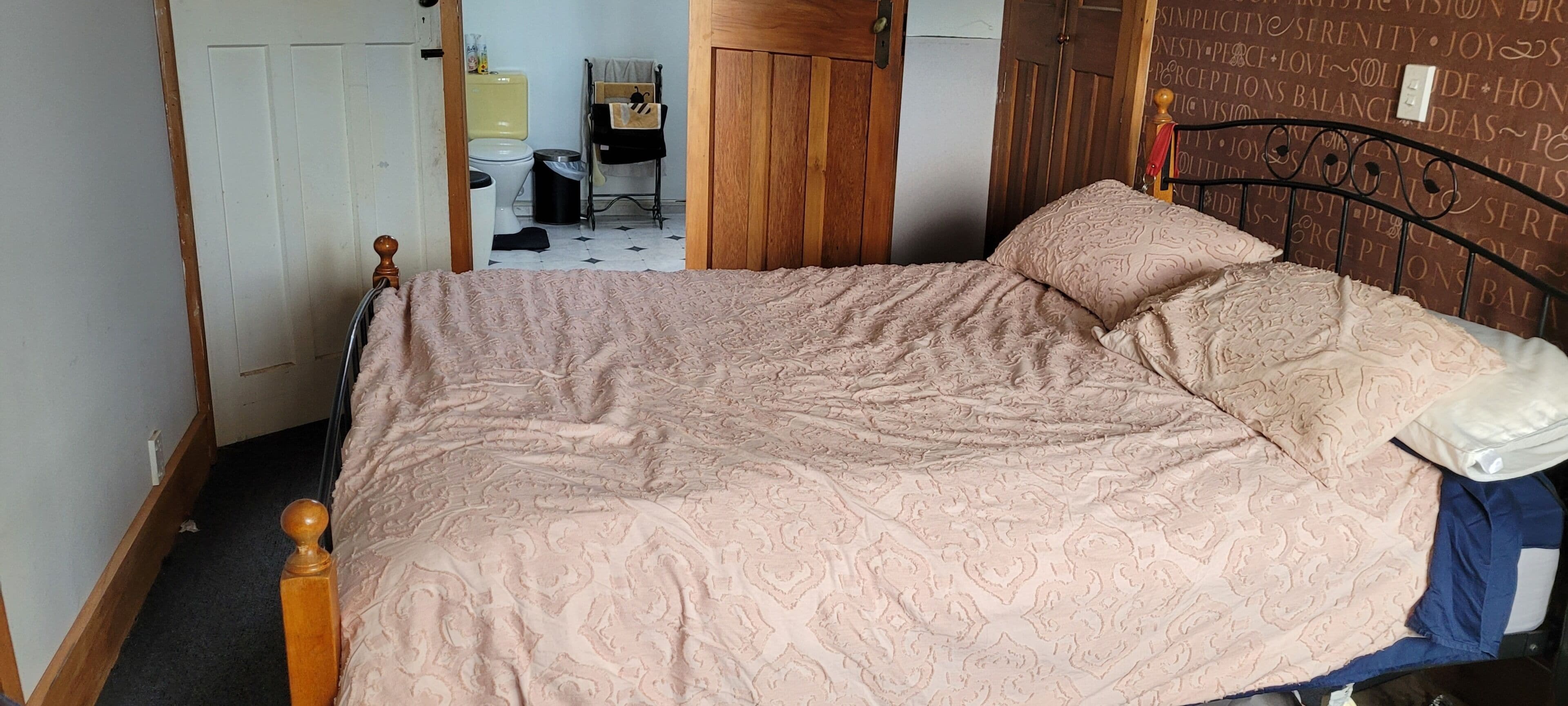 A bedroom with a bed, a wooden headboard, a bedside table, and a wall with motivational quotes.