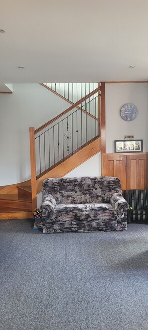 A living room with a wooden staircase, a patterned sofa, a clock, and a framed picture on the wall.