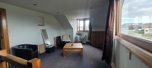 A room with a sloped ceiling, a wooden table, a black chair, a window with curtains, and a view of a residential area.