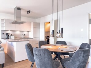 Une cuisine moderne avec un îlot central, des chaises recouvertes d’un tissu gris et des luminaires suspendus.