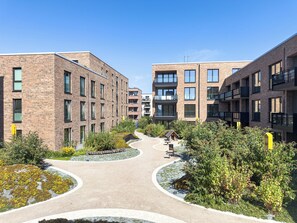 Un bâtiment moderne à étages, doté d’une cour intérieure avec des allées et entouré de verdure.