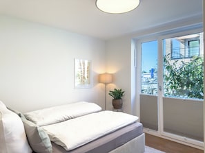 Une chambre à coucher avec un lit, une lampe, une plante et une vue sur l’extérieur.