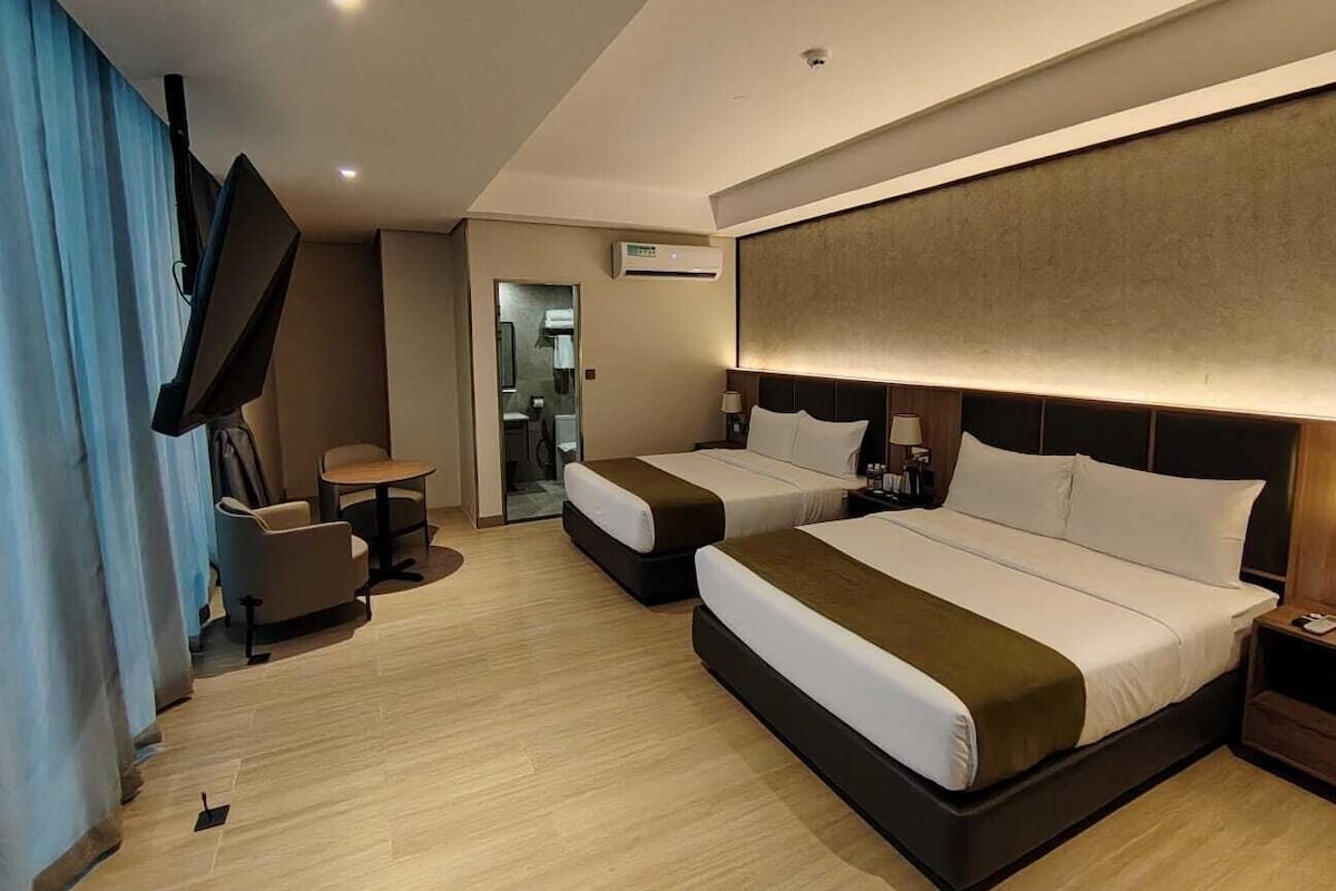 Ein Hotelzimmer mit zwei Betten, einem Fernseher, einem Schreibtisch und einem Sessel.