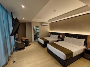 Ein Hotelzimmer mit zwei Betten, einem Fernseher, einem Schreibtisch und einem Sessel.