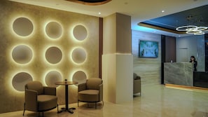 Eine moderne Lobby mit runden Wandleuchten, einem Empfangstresen und einer Sitzecke mit zwei Stühlen und einem kleinen Tisch.