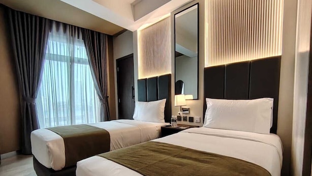 Een hotelkamer met twee bedden, een grote spiegel, een nachtkastje en een raam met gordijnen.