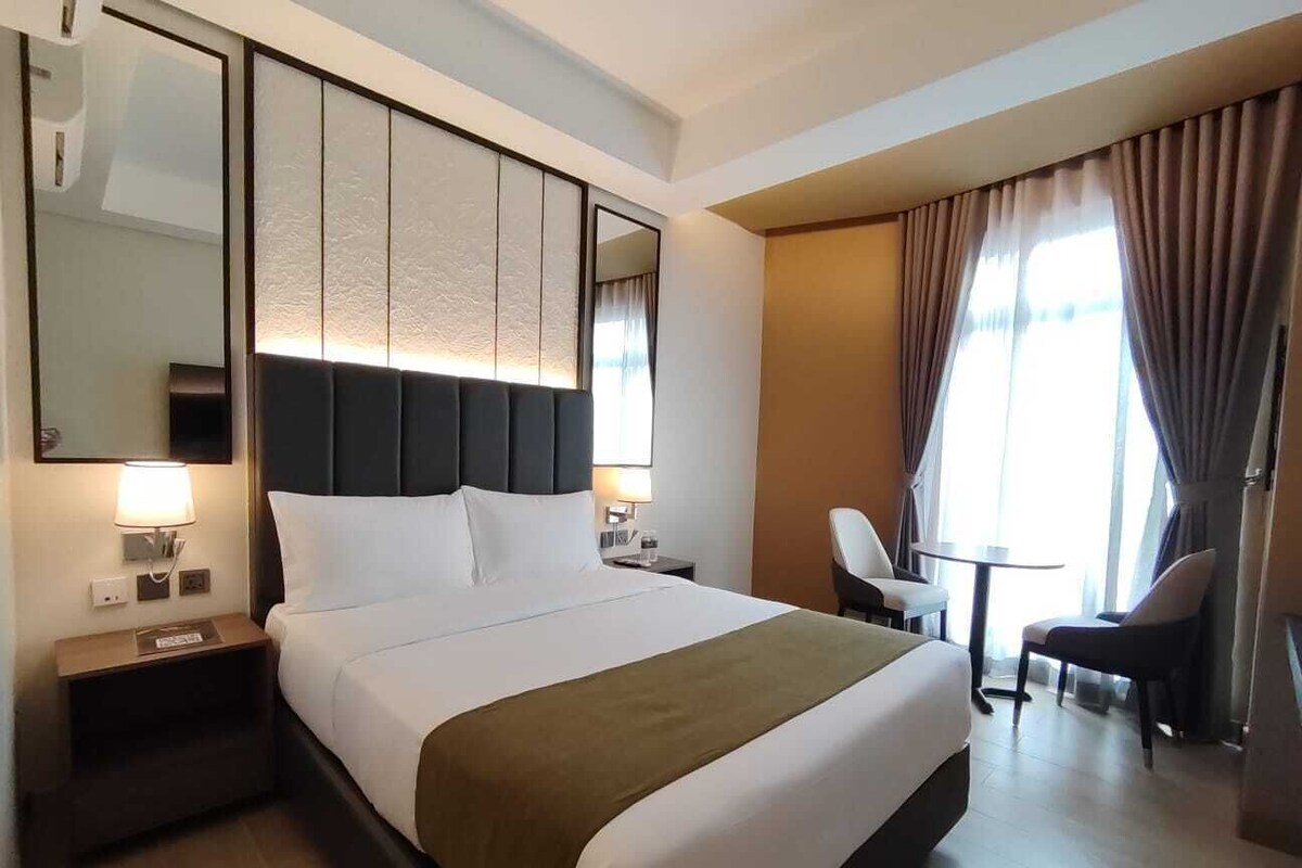 Ein Hotelzimmer mit einem großen Bett, einem Nachttisch, einem Sessel, einem kleinen Tisch und einem Spiegel.