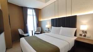 Een hotelkamer met een groot bed, nachtkastjes, een stoel en een raam met gordijnen.