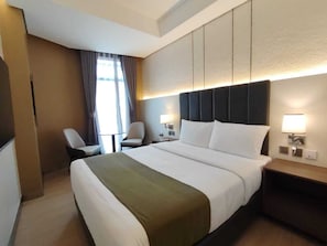 Ein Hotelzimmer mit einem großen Bett, Nachttischen, einem Sessel und einem Fenster mit Vorhängen.