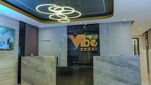 A reception area with a modern design, featuring a prominent logo and a marble reception desk. - Vibe Hotel - Buendia (Pasay)