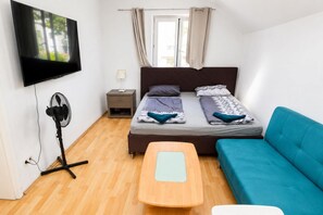 A bedroom with a bed, a TV, a fan, a bedside table, a nightstand, and a blue sofa.