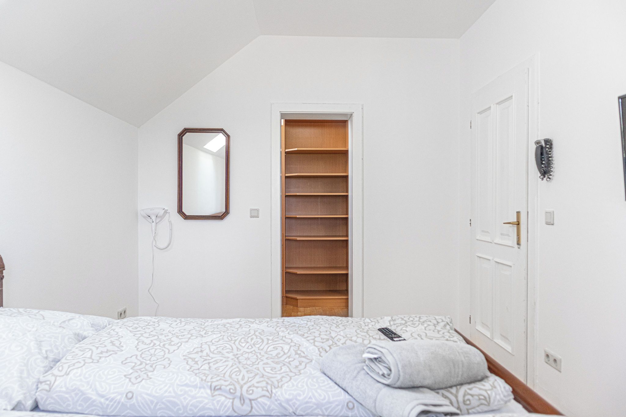Un dormitorio con una cama, un armario de madera, un espejo y una puerta con picaporte.