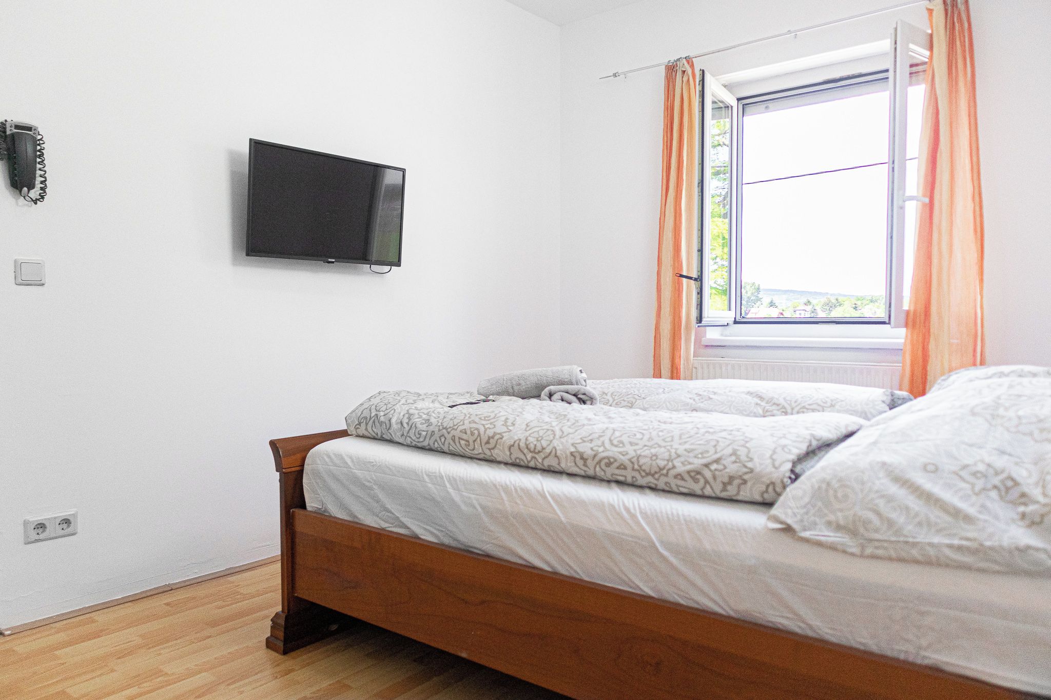 A bedroom with a bed, a television mounted on the wall, and a window with curtains.