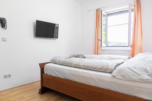 A bedroom with a bed, a television mounted on the wall, and a window with curtains.
