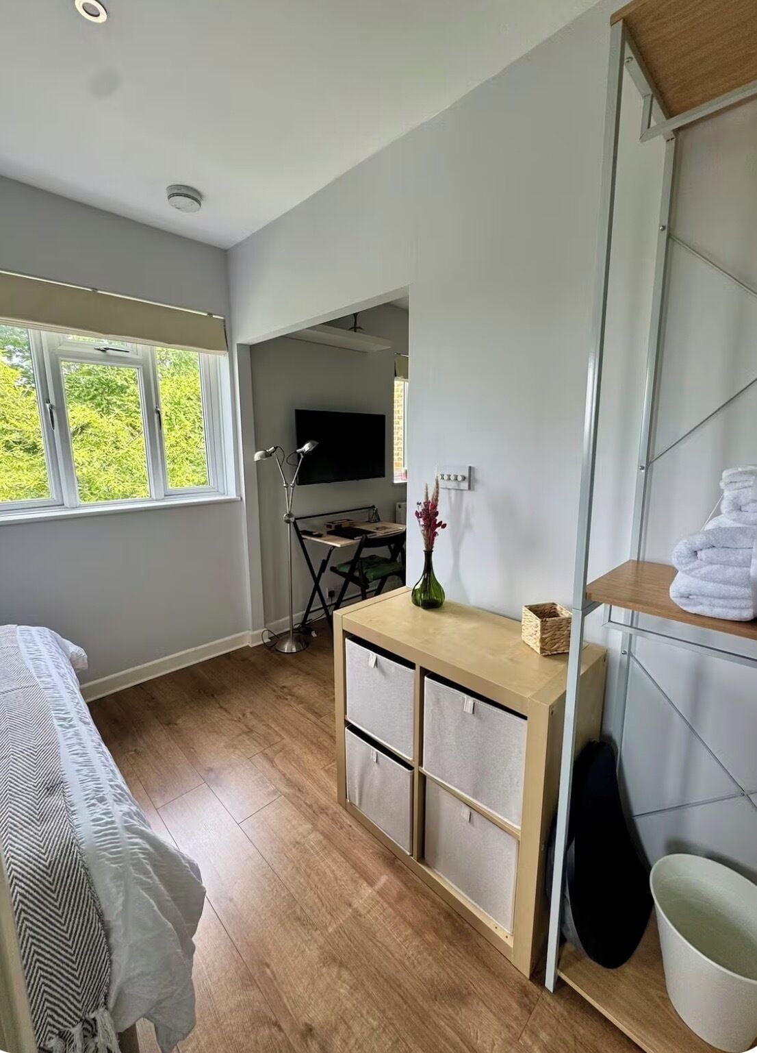A bedroom with a bed, a desk with drawers, a TV, and a window with a view of trees.