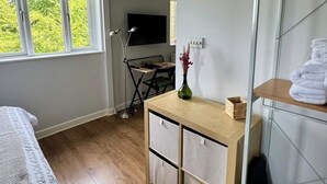 Ein Schlafzimmer mit Bett, Schreibtisch mit Schubladen, Fernseher und Fenster mit Blick auf Bäume.