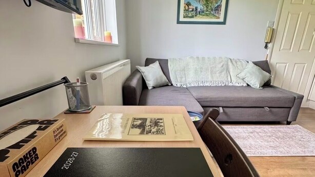 Ein Wohnzimmer mit einer Couch, einem Tisch mit einer Kiste mit der Aufschrift 'NAKED PAPER' und einem gerahmten Bild an der Wand.